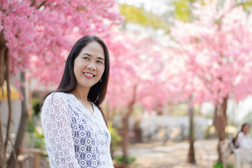 Asian middle-aged woman in white shirt standing and smiling in the rest area of private park while taking weekend vacation, soft focus, happiness of people concept.