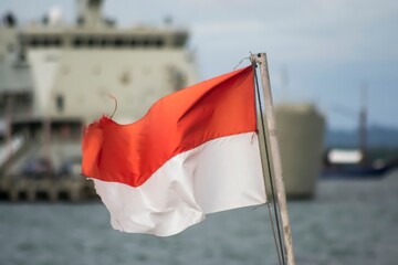 The Indonesian national flag flies against the backdrop of warships anchored at the pier