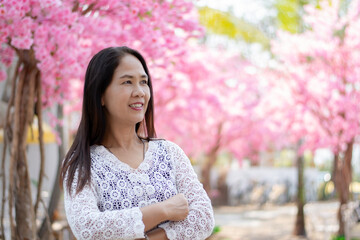 Asian middle-aged woman in white shirt standing and smiling in the rest area of private park while taking weekend vacation, soft focus, happiness of people concept.
