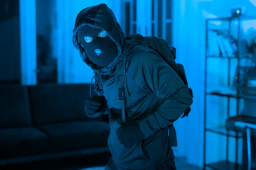 Masked man burglar ducking and hiding indoors