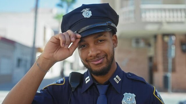 A confident african american police officer saluting outdoors in an urban setting.