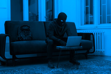 Masked hacker using laptop in dark room