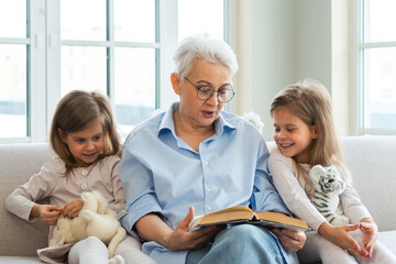 Happy family at home. Two girls sisters twins grandmother reading story book together. Good time at...