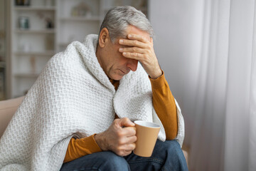 Elderly man holding a mug with a worried expression - 779095657