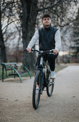 Casual teenage boy riding a bicycle on a park path, surrounded by trees in a tranquil outdoor setting.