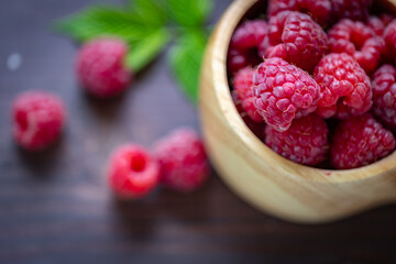 Summer harvest of ripe raspberries in the wooden bowl on a wooden table with shallow depth of field.