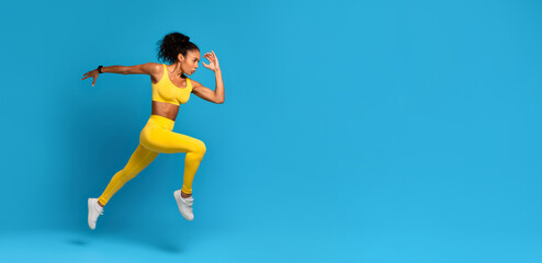 Fototapeta na wymiar Dynamic athlete black woman in mid-jump on blue background