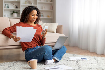 Smiling Black Woman Sitting on Floor With Laptop and Documents