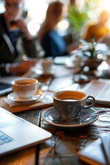 Coworkers sipping coffee together at a communal table, with laptops and paperwork scattered around