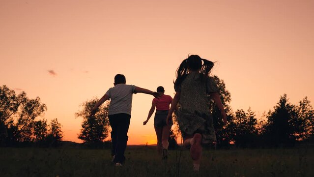 Parent of boy, girl running through meadow towards sunset sky in park. Kid son daughter play with mom on lawn. Family team, sports games, adult children. Active family, mother, children run merrily