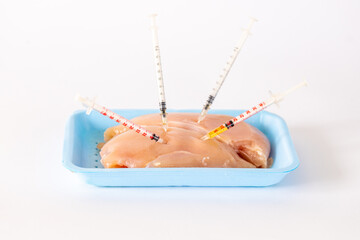 Chicken meat on a tray with syringes stuck in it, Nutrition concept, antibiotics in meat, Chemically stuffed food, White background