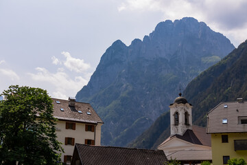 Central Parish Church and Buildings of Log pod Mangartom in Julian Alps, Bovec, Slovenia, Europe. Scenic view of mount Rombon in untamed Slovenian Alps. Majestic mountain peaks in serene Soca valley