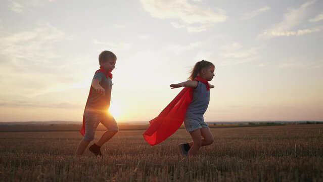 children in superhero costumes. concept of a happy childhood and family for a child. a boy and a girl with red capes and blue T-shirts are running lifestyle across a field, sunset in the background