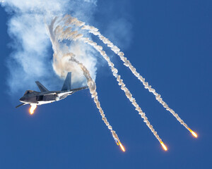 Epic frontal view of a F-22 Raptor deploying flares in a turn, in smoke and in beautiful light
