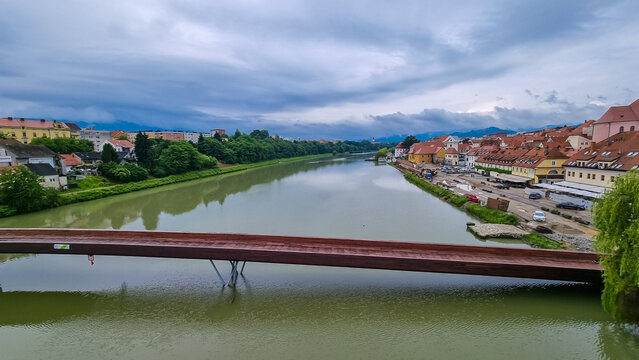 Wooden Splavarska brv bridge (Timber Rafting Footbridge) gracefully spans across majestic Drava River in enchanting city of Maribor, Slovenia. Panoramic view of the city architecture along riverbanks