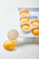 Rack for six broken eggs with whole yolks. One egg lies nearby, the yolk is on the table