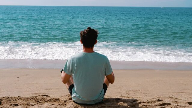A man meditates on the sand against the backdrop of the sea. Knowing yourself