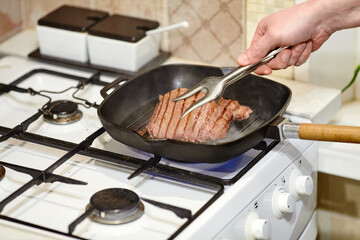 The process of cooking two beef steaks in frying pan, the hands of male chef salting raw meat, close-up