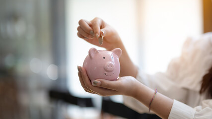Close-up of a person depositing a coin into a pink piggy bank, savings and financial planning.