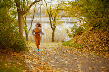 Full length portrait of woman in fitness clothes in park jogging - 779125041