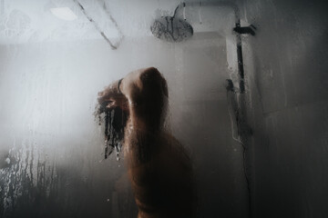 A contemplative mood emanates from the silhouette of a lone person, obscured by the mist of a hot shower.