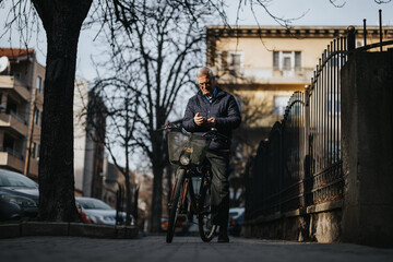 Mature man checks phone messages in quiet street, with bike. Image evokes urban lifestyle, active seniors and sustainable transportation.