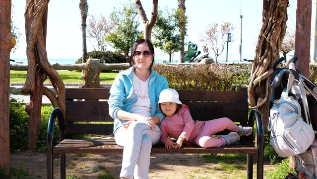 Mom and child are relaxing in the park. They are sitting on a bench. Summer day