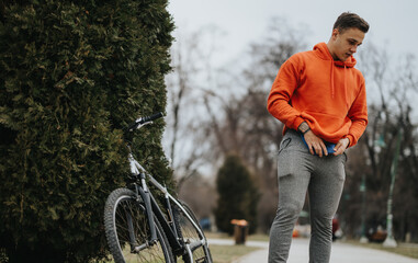 A young, active man pauses next to his bicycle in a tranquil park on a cloudy day, embodying a...