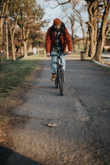 Fototapeta premium Casual young adult riding a bicycle on a park pathway surrounded by trees in the soft afternoon light.