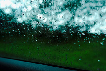 Rain drops on car window, rainy day. Green background outside