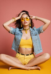 A confident young Indian supermodel woman in a cropped yellow top, white shorts, and fashionable accessories strikes a striking pose.
