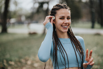 A cheerful teenage girl with braids and braces holding a daisy in the park, dressed in sporty blue attire, representing youthful energy and a healthy lifestyle.