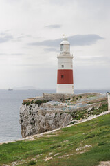 Fototapeta na wymiar A lighthouse is on a rocky cliff overlooking the ocean. The lighthouse is red and white. The ocean is calm and the sky is cloudy