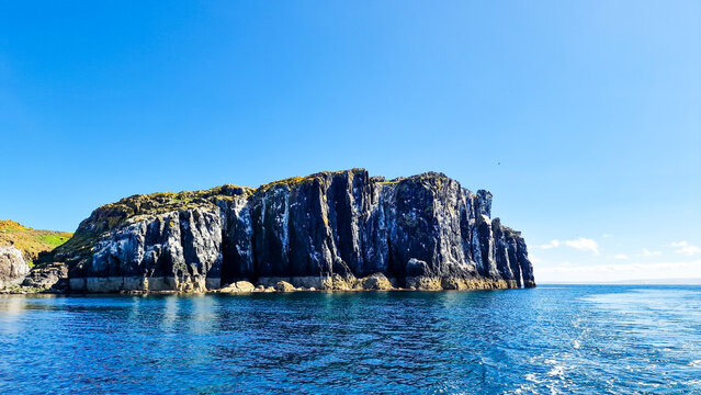 Majestic multi coloured rocky cliffs of the Isle with green terrain surrounded by appealing blue-green sea and the clear sky, Isle of May Natural Nature Reserve, Scotland, UK