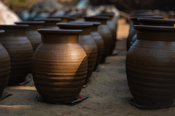 Earthen mud pots placed in rows for drying during morning. Sunlight on the mud pot. Selective focus.