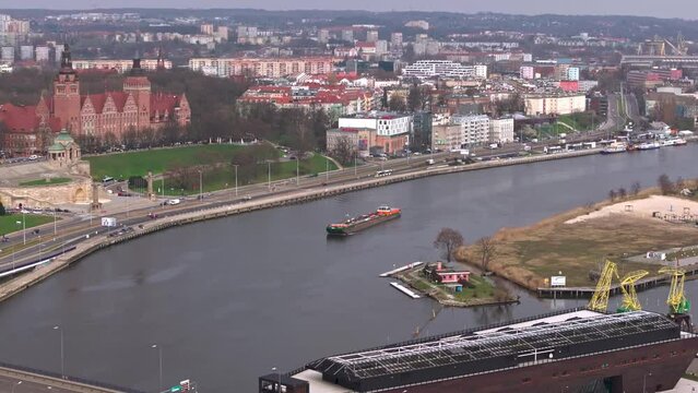 Cargo ship gliding along West Oder by Chrobry Embankments and National Museum in Szczecin, captured  by drone.