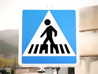 Pedestrian crossing sign on a village street closeup. Blue square traffic sign with a person on a crosswalk