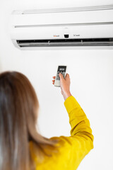 Woman holding remote control aimed at the air conditioner.