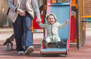 A beautiful, cheerful little boy of two years old walks with his mother on the playground in the...