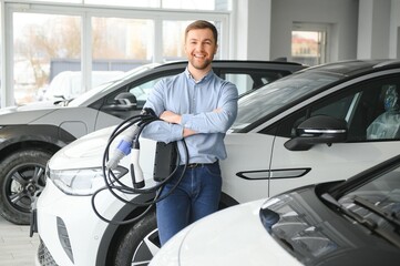 A happy man chooses a new electric car at a car dealership. The concept of buying an ecological car