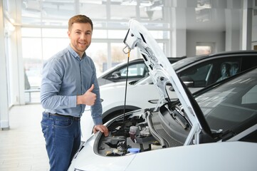 Concept of buying electric vehicle. Handsome business man stands near electric car at dealership