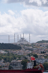 Camlica Mosque with its six minarets, seen from a boat on the Bosphorus, in the foreground a cargo ship with a Turkish boat and residential buildings on the hill, vertical