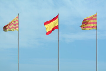 The image captures a moment of peaceful coexistence, with the flags of Catalonia and Spain waving together under a clear blue sky, reflecting cultural and political diversity.