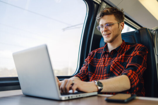 A traveler in train near window is typing on a laptop while commuting.
