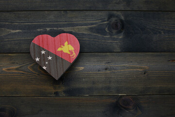 wooden heart with national flag of Papua New Guinea on the wooden background.