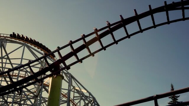 People riding on extreme rail roller coaster attraction in amusement park at sunset.