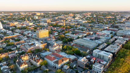 Naklejka premium Golden sunrise light bathes downtown Charleston, South Carolina, with historic buildings and streets visible from an aerial view.
