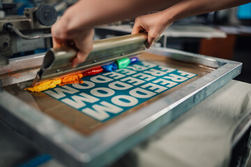 Graphic worker's hands pressing ink with squeegee and screen printing.