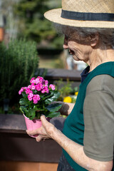 Elderly woman tending to colorful flowers on a sunny patio - 779202878