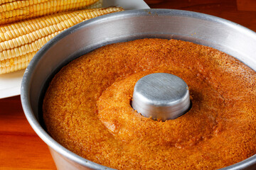 corn cake in the pan baking form on rustic wooden table. Typical Brazilian party food. Selective focus